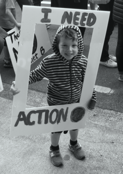 Image of a child holding a picture frame upon which is written 'I NEED ACTION'